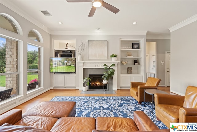 living area featuring a warm lit fireplace, built in shelves, visible vents, and crown molding