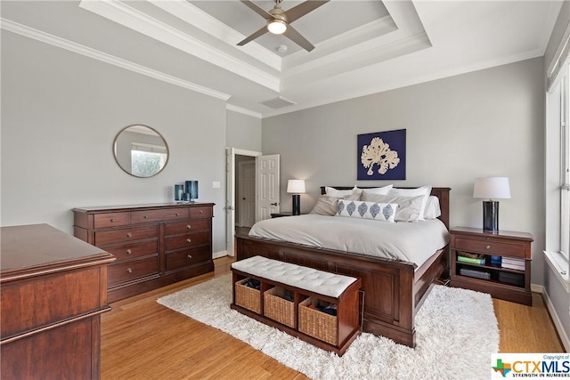 bedroom with visible vents, ceiling fan, ornamental molding, a tray ceiling, and light wood-type flooring