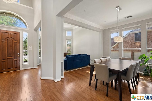 dining area featuring a high ceiling, visible vents, baseboards, wood-type flooring, and crown molding