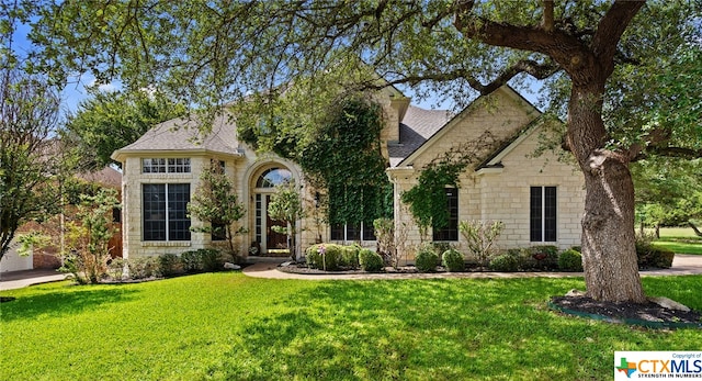 view of front of house featuring a shingled roof, stone siding, and a front lawn