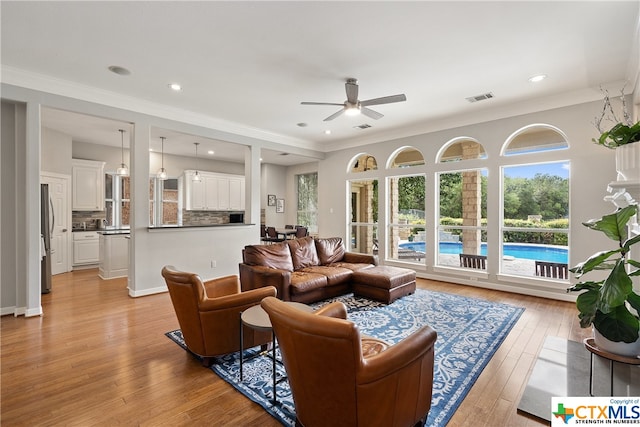 living area featuring ceiling fan, recessed lighting, visible vents, ornamental molding, and light wood-type flooring