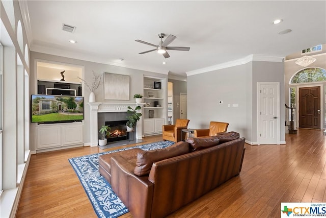 445 Champions Dr, Georgetown, TX 78628 - living area with ornamental molding, ceiling fan, a lit fireplace, light wood finished floors, and recessed lighting