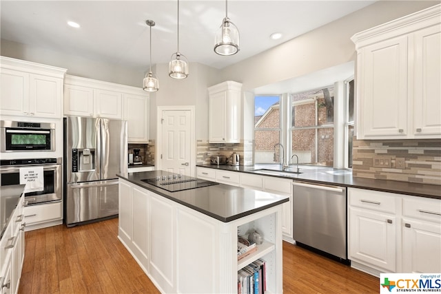 kitchen featuring a center island, stainless steel appliances, dark countertops, white cabinetry, and a sink