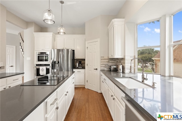 kitchen with stainless steel appliances, dark countertops, tasteful backsplash, white cabinetry, and a sink