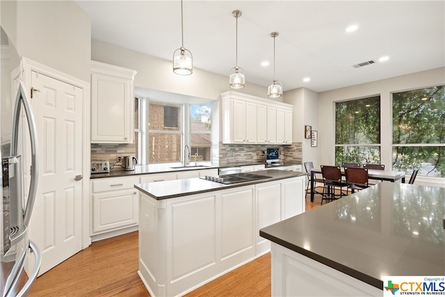 kitchen with dark countertops, a kitchen island, light wood-type flooring, stainless steel refrigerator with ice dispenser, and a sink