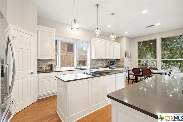 kitchen featuring dark countertops, light wood-style floors, a sink, a kitchen island, and stainless steel fridge with ice dispenser