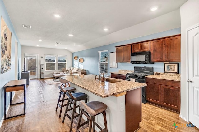 kitchen featuring visible vents, a breakfast bar area, light wood-style floors, black appliances, and a sink