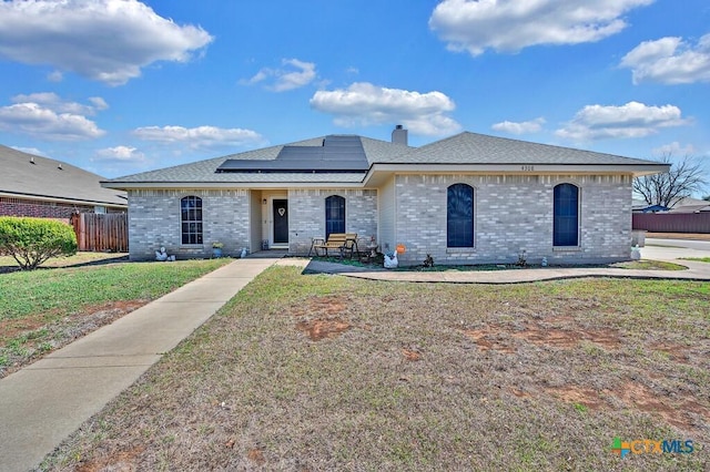 view of front of house featuring brick siding, solar panels, a chimney, and a front yard