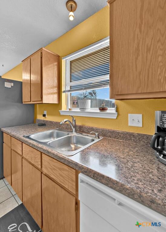 kitchen featuring a sink, dark countertops, dishwasher, and light tile patterned flooring