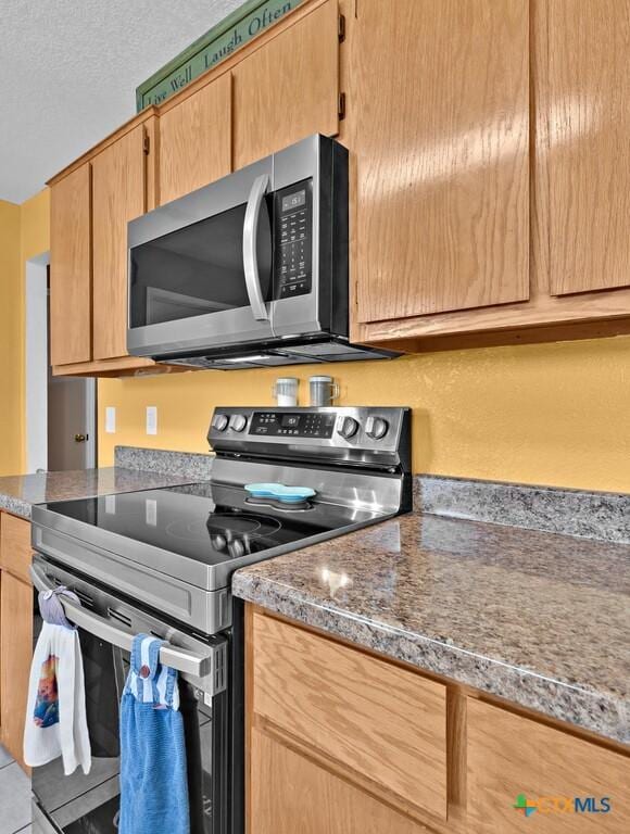 kitchen featuring dark stone countertops, stainless steel appliances, a textured ceiling, and tile patterned flooring