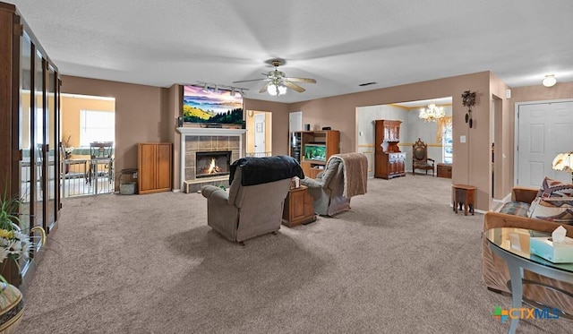 carpeted living area with a tiled fireplace, ceiling fan with notable chandelier, and visible vents