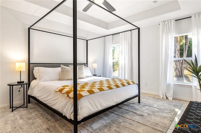 tiled bedroom with a raised ceiling, ceiling fan, and multiple windows