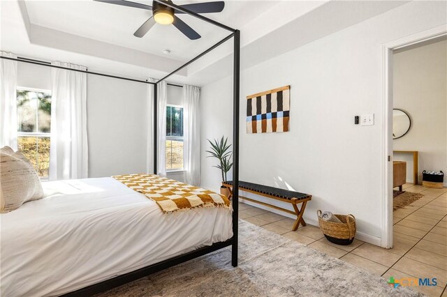 bedroom with ceiling fan, a tray ceiling, and light tile patterned floors