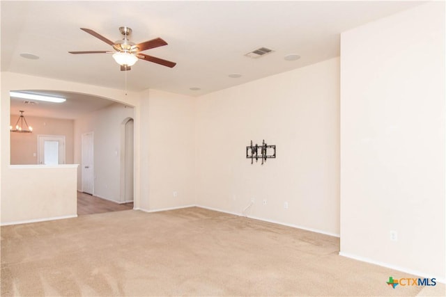 empty room featuring arched walkways, light colored carpet, a ceiling fan, baseboards, and visible vents