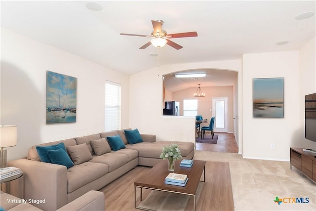 living area featuring a wealth of natural light, light colored carpet, vaulted ceiling, and arched walkways