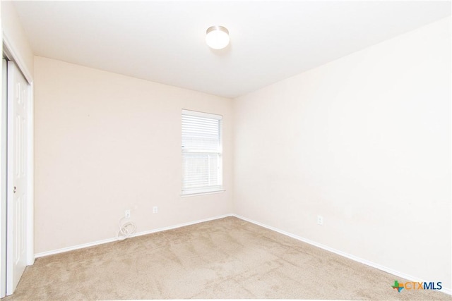 unfurnished bedroom with a closet, light colored carpet, and baseboards