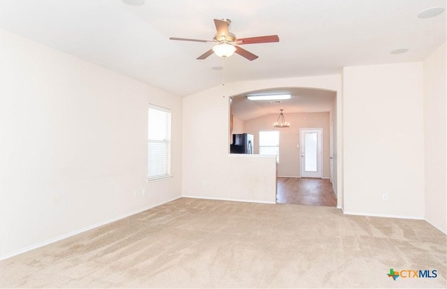 spare room with light carpet, arched walkways, baseboards, lofted ceiling, and ceiling fan with notable chandelier