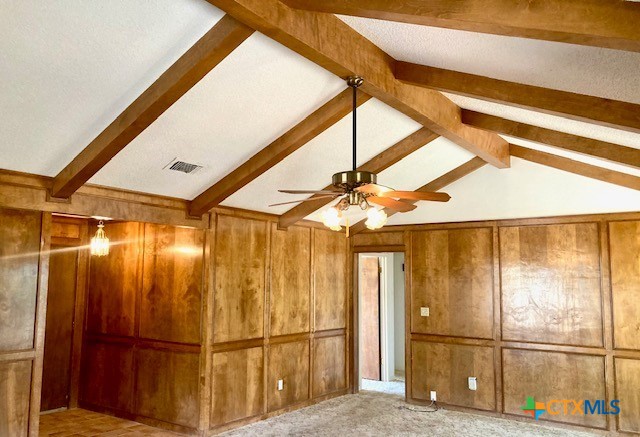 interior space with lofted ceiling with beams, ceiling fan, light carpet, and wooden walls