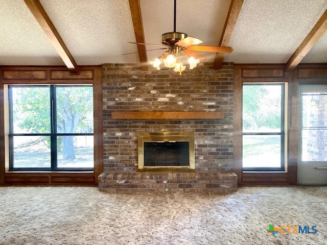 unfurnished living room with a brick fireplace, a textured ceiling, beamed ceiling, and carpet flooring