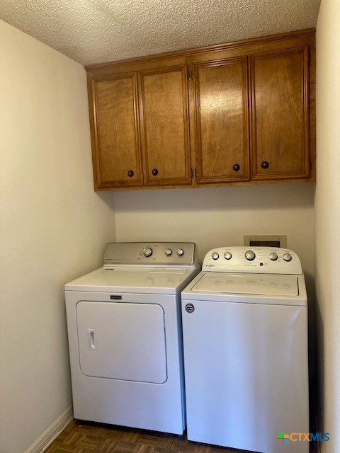 laundry area with cabinets, dark parquet flooring, washing machine and dryer, and a textured ceiling