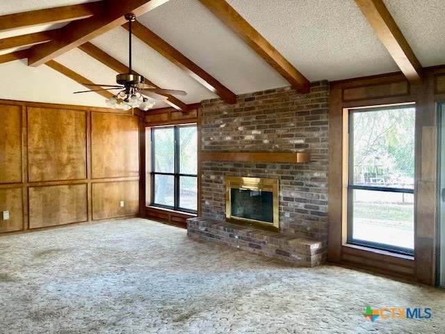 unfurnished living room with vaulted ceiling with beams, wood walls, a brick fireplace, a textured ceiling, and carpet floors