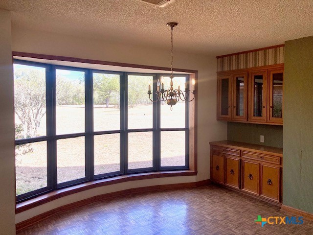 unfurnished dining area with parquet floors, a notable chandelier, and a textured ceiling