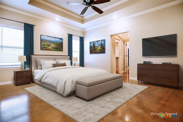 bedroom with ornamental molding, light wood-type flooring, a tray ceiling, and ceiling fan