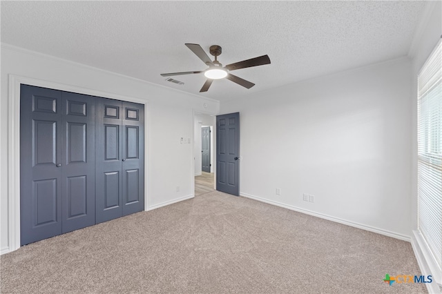 unfurnished bedroom featuring a closet, a textured ceiling, light colored carpet, and ceiling fan