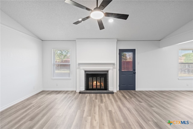 unfurnished living room featuring a wealth of natural light, vaulted ceiling, light hardwood / wood-style floors, and a textured ceiling