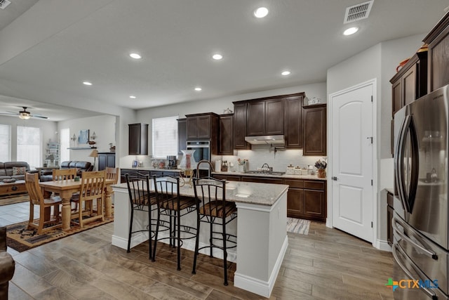 588 Vale Ct, New Braunfels, TX 78132 - kitchen featuring appliances with stainless steel finishes, ceiling fan, a breakfast bar area, a kitchen island with sink, and light wood-type flooring