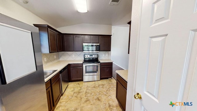 kitchen with dark brown cabinetry, sink, lofted ceiling, decorative backsplash, and appliances with stainless steel finishes