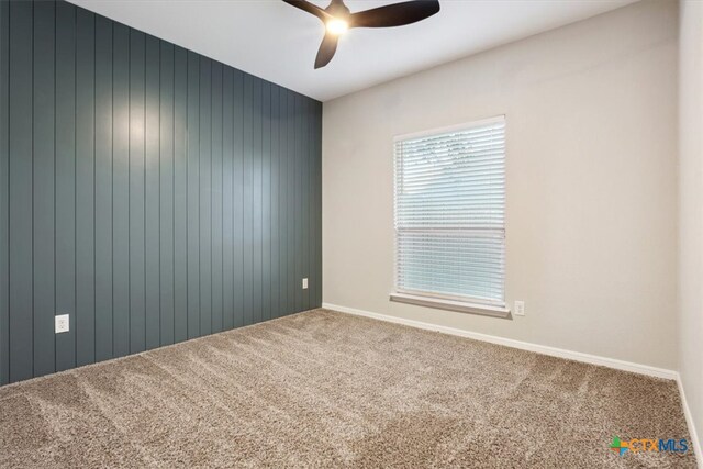 carpeted empty room featuring wooden walls and ceiling fan