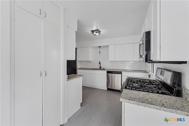 kitchen featuring backsplash, white cabinets, sink, light stone counters, and stainless steel appliances