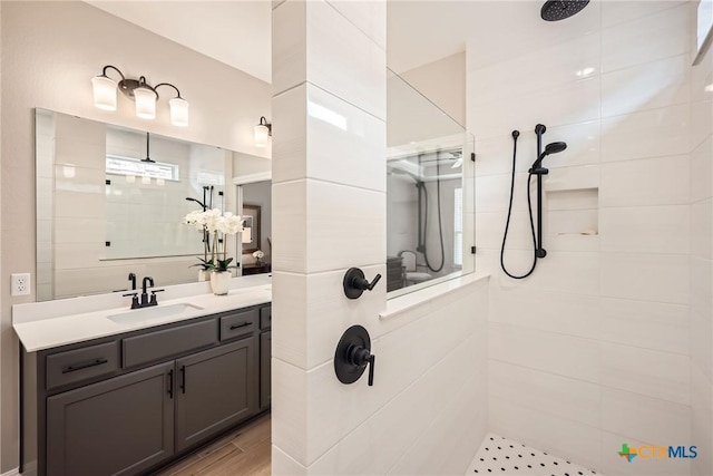 bathroom featuring a tile shower, wood finished floors, and vanity