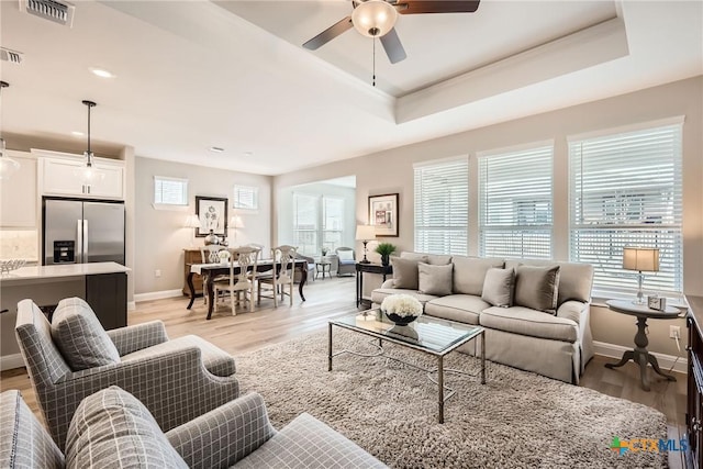 living area featuring light wood-style floors, a tray ceiling, and visible vents