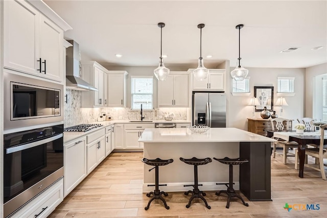 kitchen with stainless steel appliances, a sink, light countertops, wall chimney range hood, and a center island