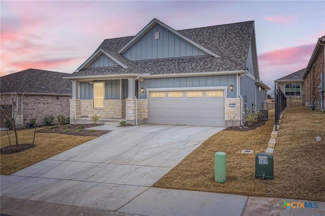 view of front facade with a shingled roof, concrete driveway, an attached garage, board and batten siding, and stone siding