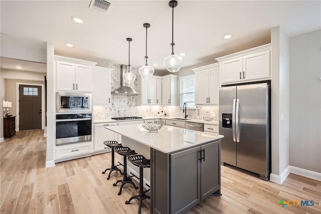 kitchen with visible vents, white cabinets, appliances with stainless steel finishes, wall chimney range hood, and a sink