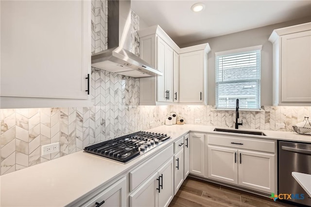 kitchen with decorative backsplash, wall chimney exhaust hood, appliances with stainless steel finishes, white cabinetry, and a sink