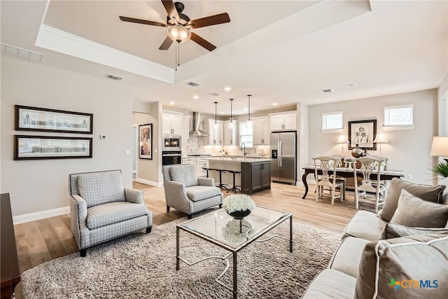 living area with light wood finished floors, baseboards, visible vents, and a raised ceiling