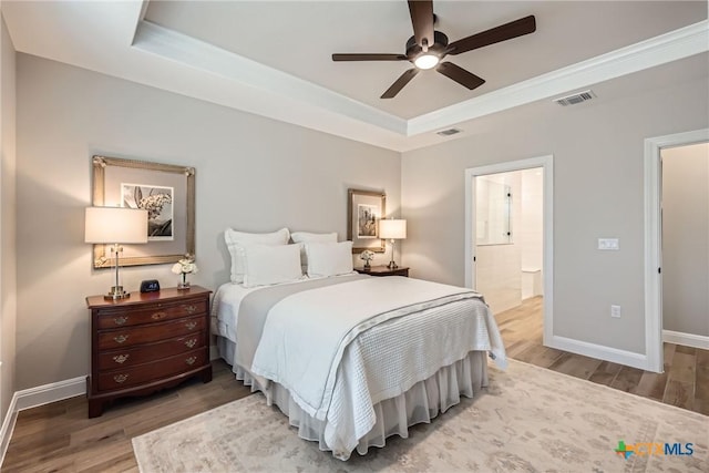 bedroom with baseboards, visible vents, a tray ceiling, and wood finished floors