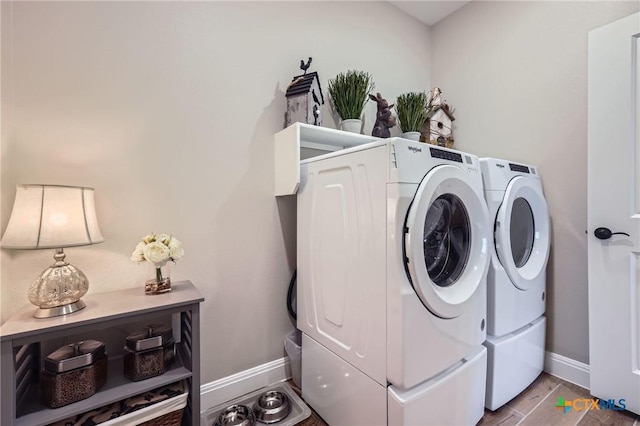 clothes washing area featuring laundry area, wood finished floors, washing machine and clothes dryer, and baseboards