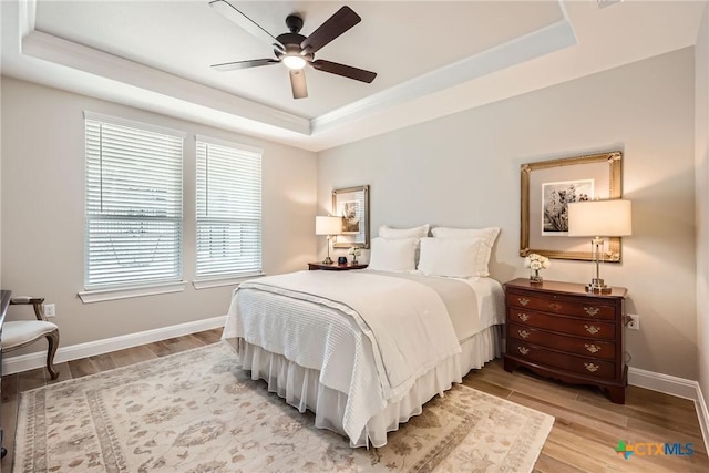 bedroom with light wood finished floors, ceiling fan, a tray ceiling, and baseboards