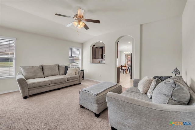 living room with arched walkways, light colored carpet, baseboards, and ceiling fan with notable chandelier