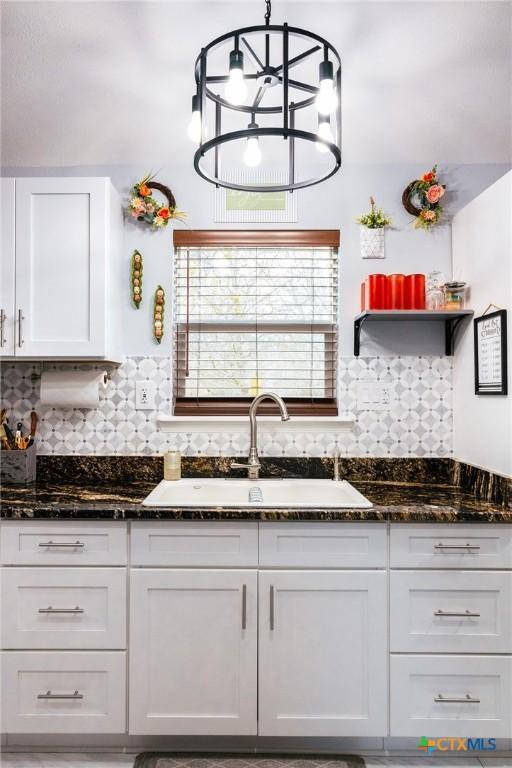 kitchen with dark stone counters, white cabinets, sink, tasteful backsplash, and decorative light fixtures