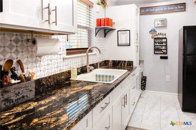 kitchen featuring white cabinetry, dark stone countertops, black refrigerator, and sink