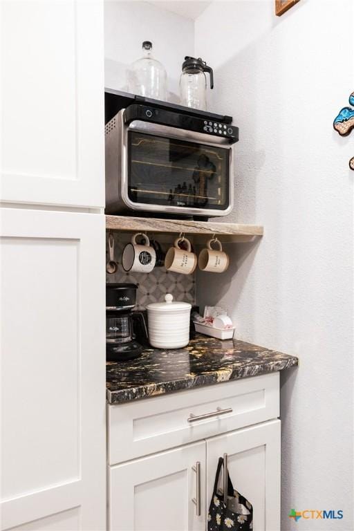 bar with white cabinets and dark stone counters