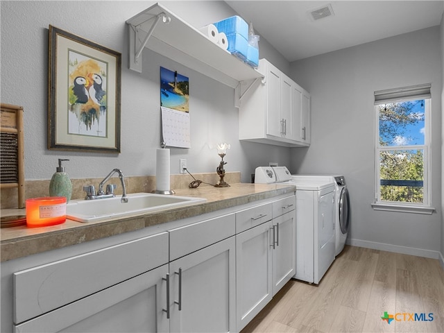 laundry room with visible vents, light wood-style flooring, washer and dryer, cabinet space, and a sink