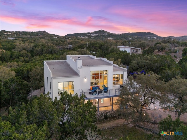 back of house at dusk with a balcony, a mountain view, and stucco siding