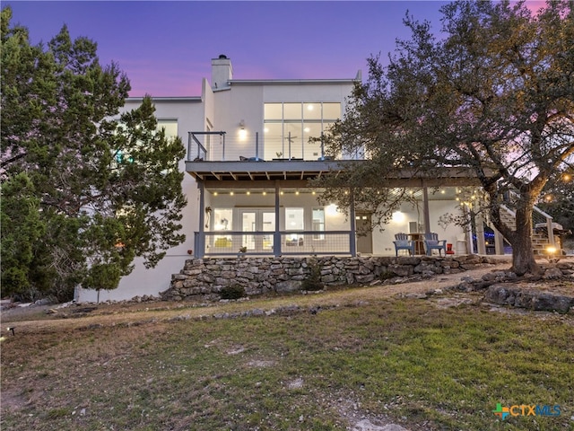 back of house at dusk featuring stucco siding, a lawn, and a chimney